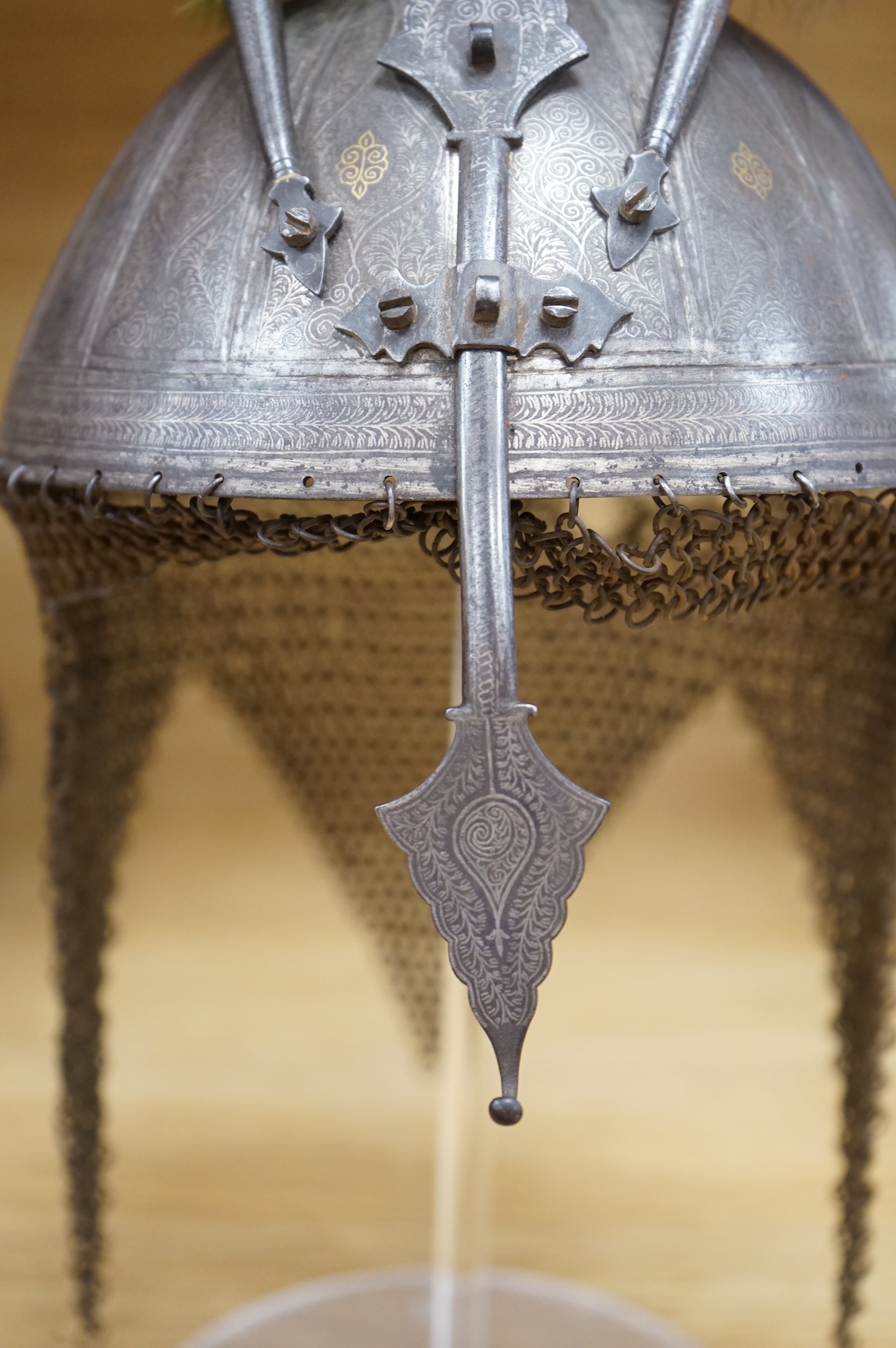 A mid to late 19th century Indian helmet and matching shield, covered with silver koftgari decoration, the helmet with sliding nasal bar and twin plume sockets surmounted by a third plume socket, the skull fluted like a